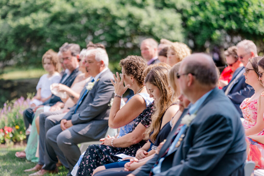 Candid wedding photo of emotional guest wiping away tears during an outdoor ceremony at Smith Farm Gardens.