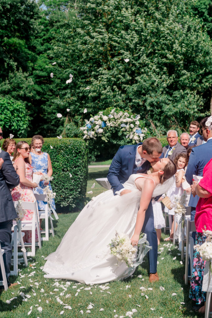 Romantic dip kiss under a shower of petals during the couple’s joyful wedding recessional at Smith Farm Gardens.