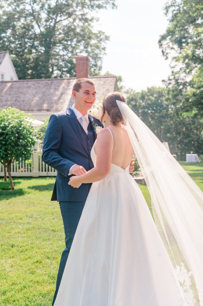 Groom smiles with joy during the couple’s first look in the gardens at Smith Farm Gardens, with the bride holding a white floral bouquet.