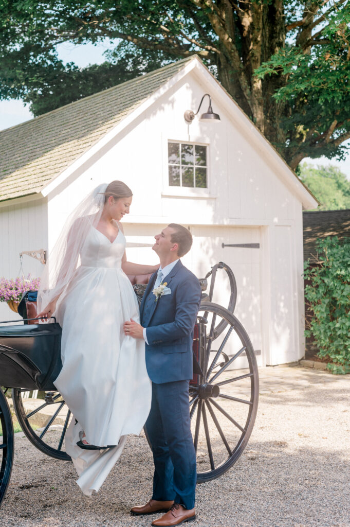 Elegant heirloom-inspired wedding moment as groom assists bride into carriage at Smith Farm Gardens in Connecticut.