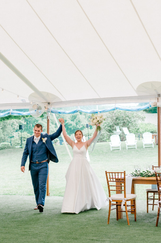 Alexis and Doug make their reception entrance, holding hands in celebration under their elegant white tent.