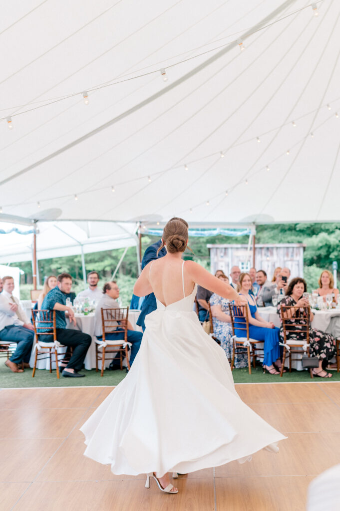 Bride spinning gracefully on the dance floor, her white gown flowing, while guests watch from their tables under the reception tent.
