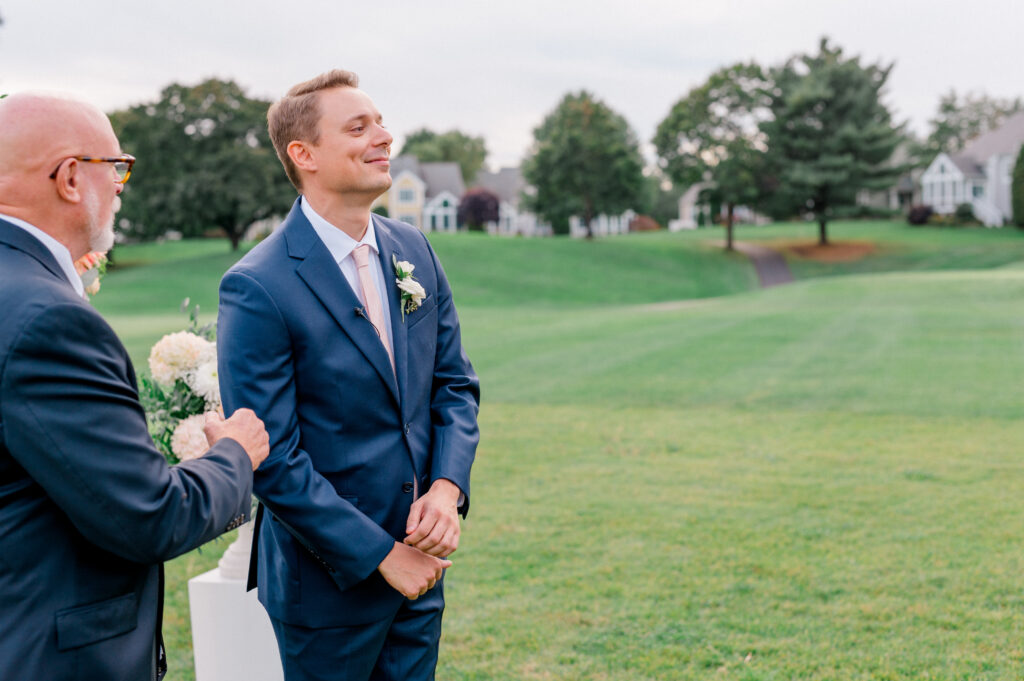 Groom smiling with emotion as he waits for the bride during a candid outdoor wedding ceremony at TPC River Highlands, photographed by Jennifer Nichole & Co.