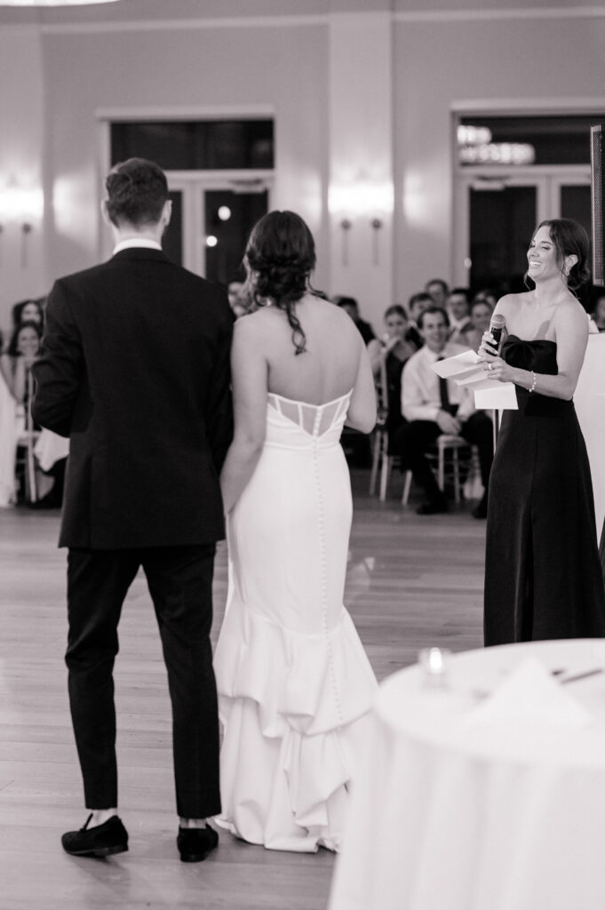 Bride and groom listening to bridesmaid giving a speech during toasts, a key moment in a Newport wedding documented by Jennifer Nichole Photography.