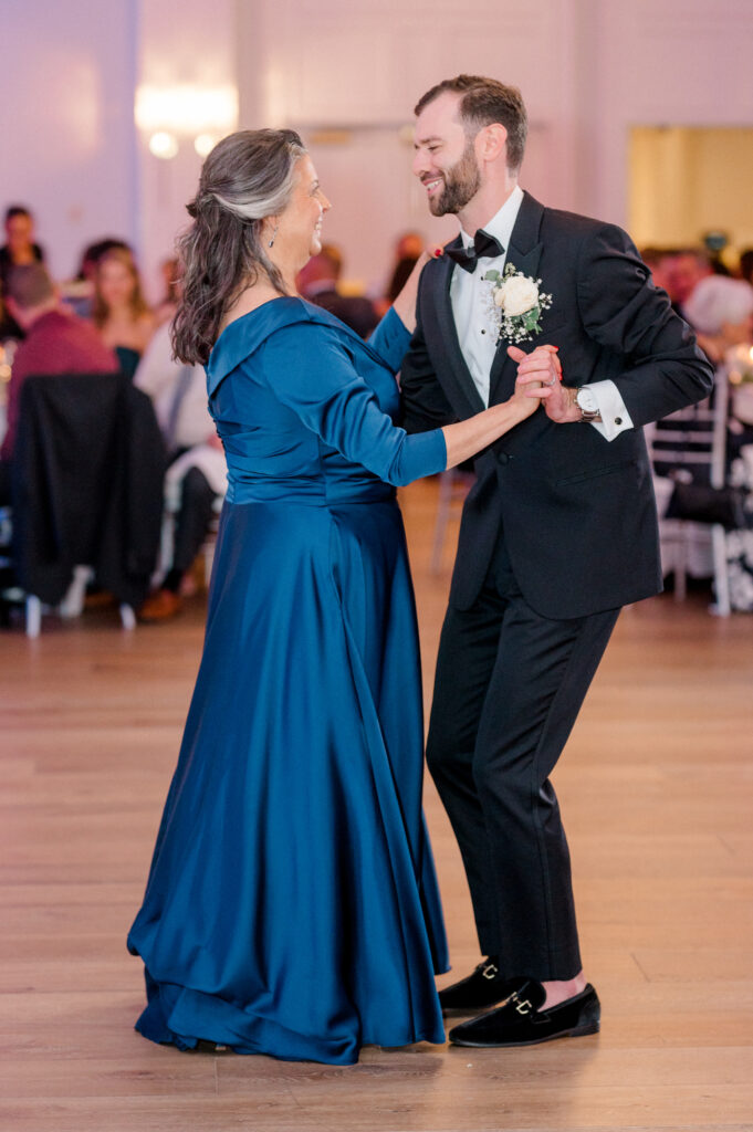 Groom smiling while dancing with his mother during mother-son dance, an emotional highlight in a Newport  wedding photographed by Jennifer Nichole.