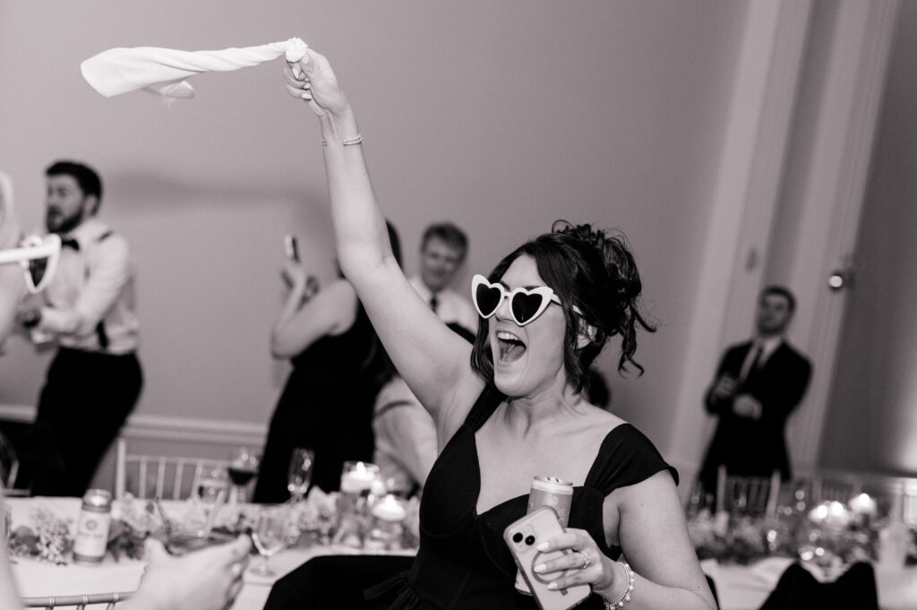 Candid moment of guest celebrating with sunglasses and waving a napkin during Newport Harbor Island wedding reception.