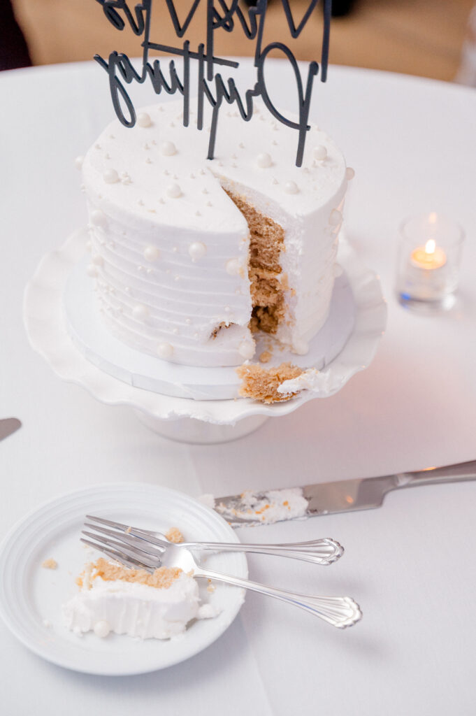 Classic white wedding cake with pearl details and a slice cut, photographed during Newport Harbor Island wedding reception.
