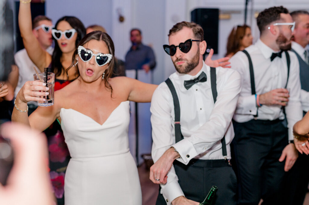 Bride and groom dancing in heart-shaped sunglasses at their Newport Harbor Island wedding reception