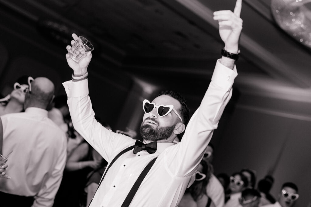 Groom cheering and dancing in heart-shaped sunglasses during reception at Newport Harbor Island Resort.