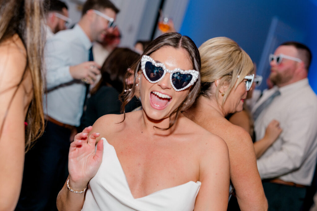 Joyful candid of bride laughing on the dance floor in pearl-trimmed sunglasses at her Newport Harbor Island wedding.