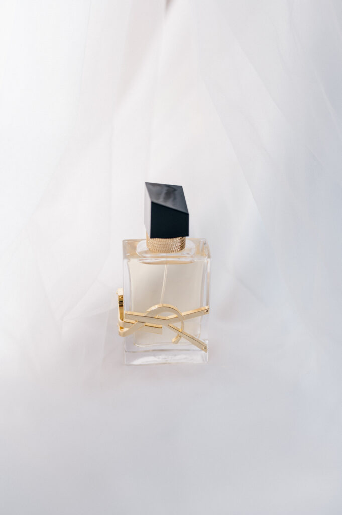 Minimalist perfume bottle with gold detailing styled on soft tulle, captured as part of wedding detail flatlay by Jennifer Nichole Photography.