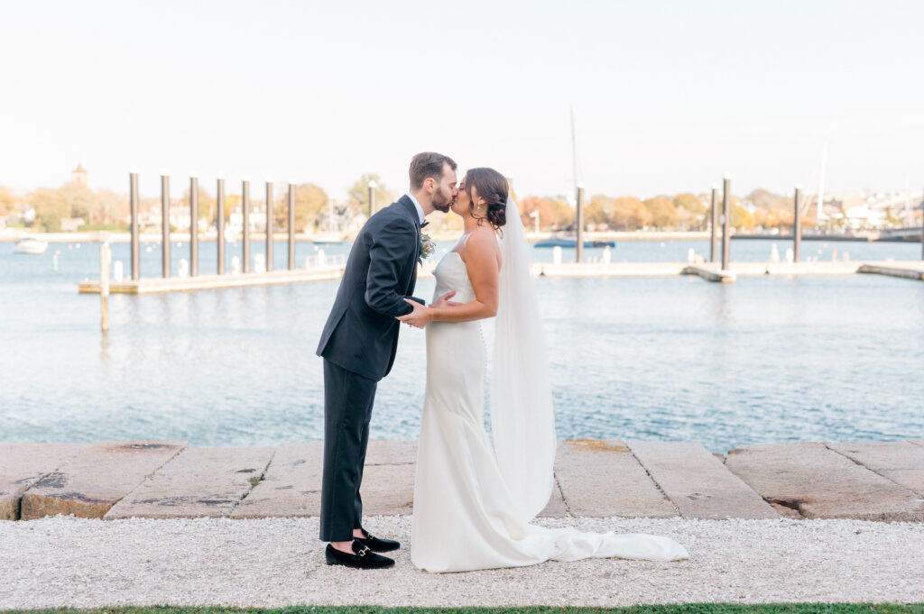 Bride and groom kiss during their first look with coastal views and fall foliage in the background at Newport Harbor Island Resort.