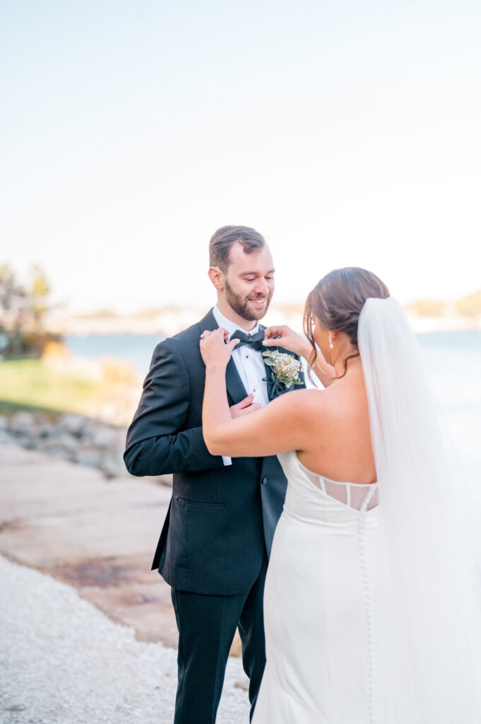 Bride sweetly adjusting the groom’s bowtie with smiles during their first look at Newport Harbor Island Resort.