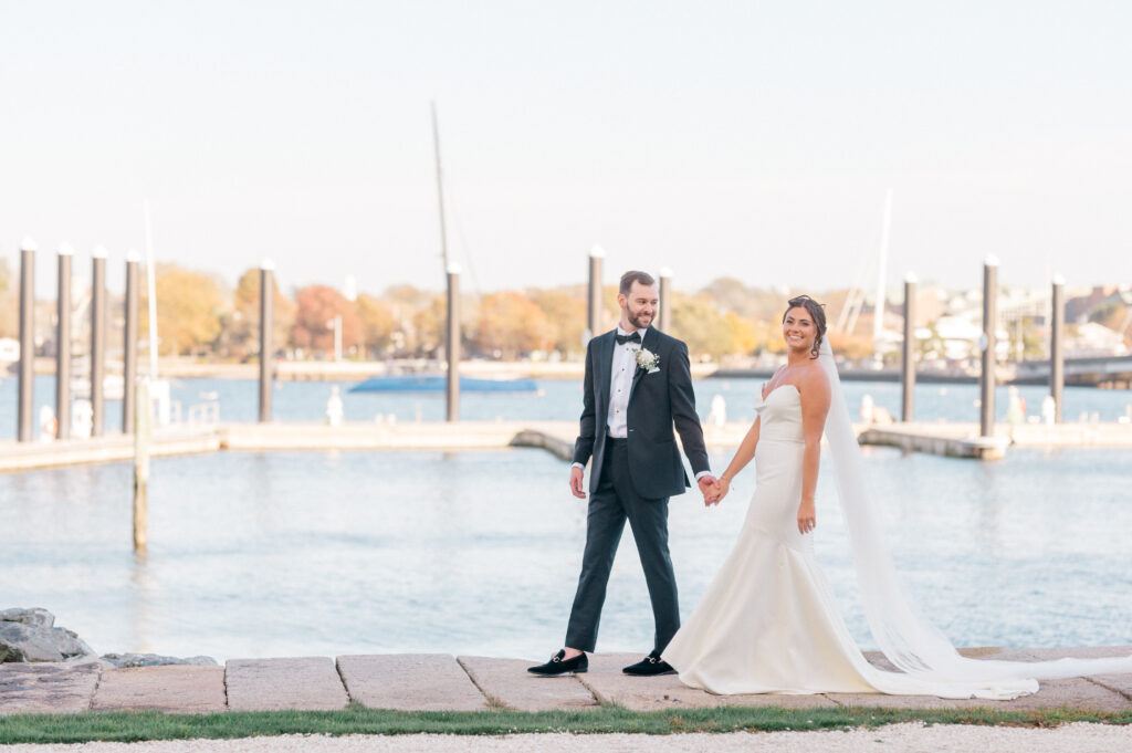 Bride and groom holding hands along the waterfront at Newport Harbor Island Resort during golden hour wedding portraits