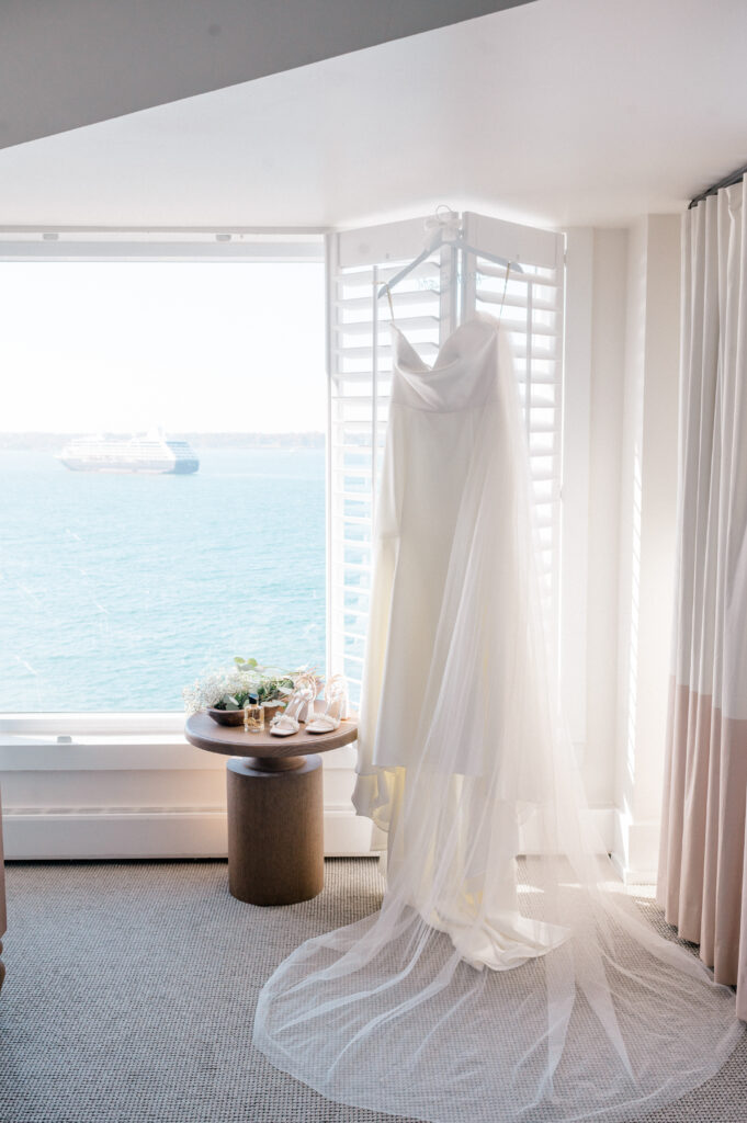 Bridal gown with flowing train and veil hanging in front of panoramic harbor view at Newport Harbor Island wedding