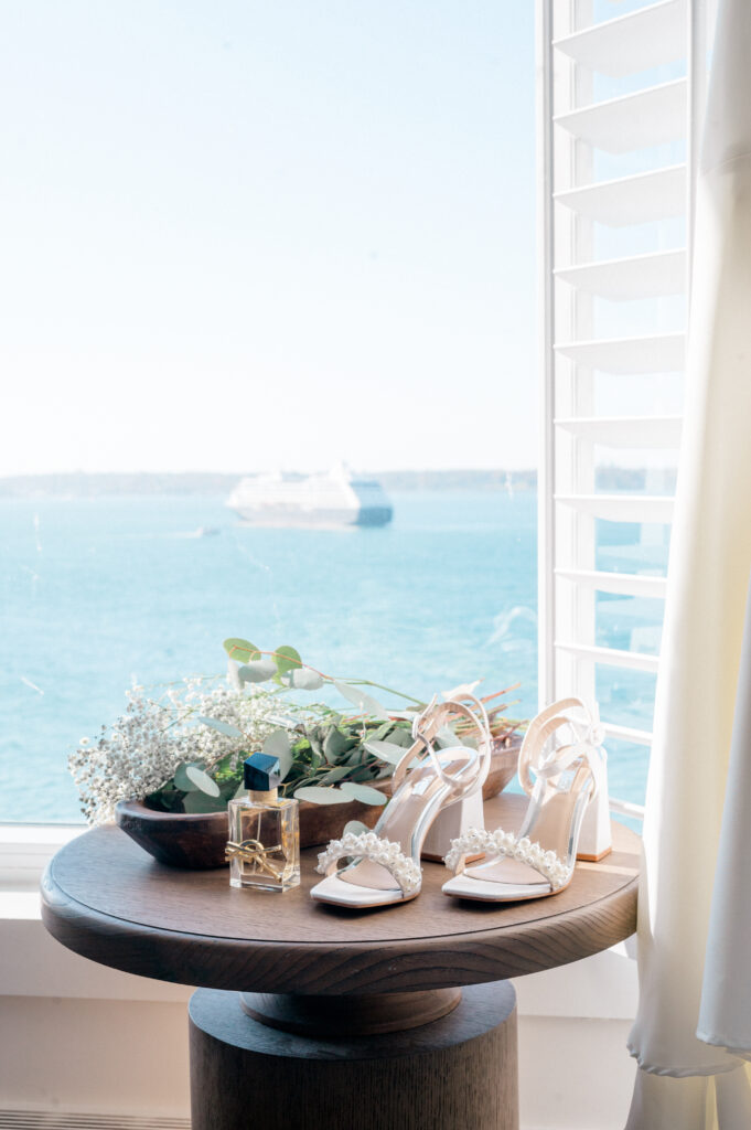 White satin heels, eucalyptus bouquet, and perfume bottle styled on a round table with ocean view at Newport Harbor Island Resort
