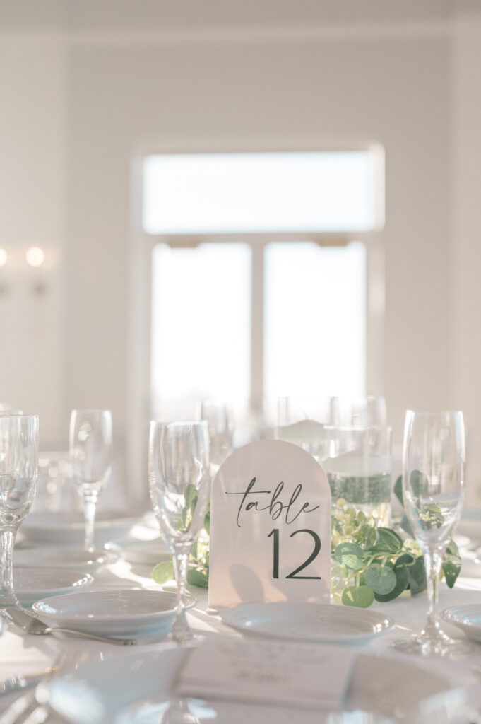 Elegant coastal wedding table decor with greenery garland, minimal signage, and natural light at Newport Harbor Island wedding.