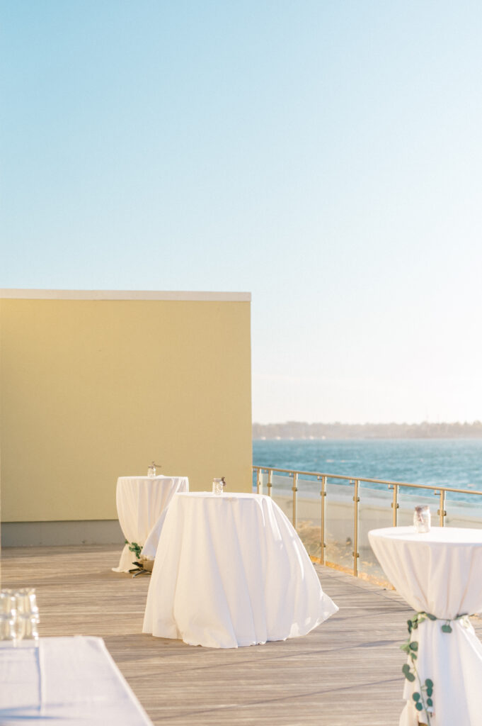 Coastal cocktail hour setup on the deck at Newport Harbor Island Resort with ocean views and white draped tables.