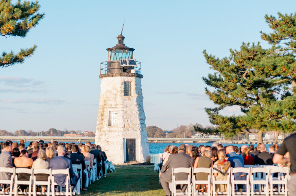 Wedding guests seated in white chairs face the lighthouse for a scenic outdoor ceremony at Newport Harbor Island Resort.