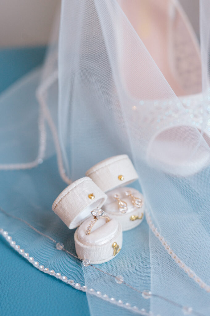 Ivory velvet ring boxes with diamond engagement ring and teardrop earrings styled under a delicate beaded bridal veil.