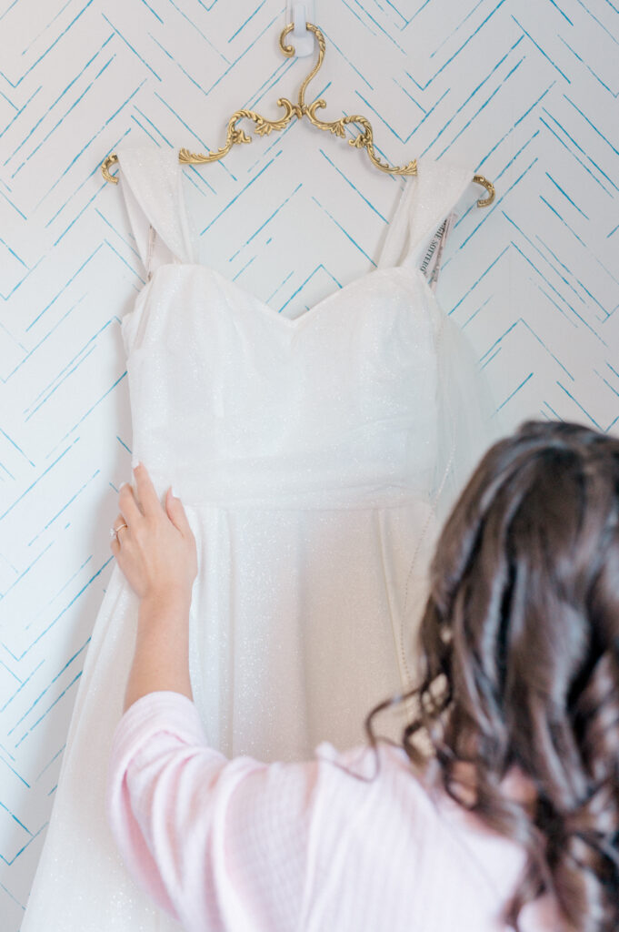 Bride admiring wedding dress hanging on ornate gold hanger, captured as part of Connecticut wedding photography timeline bridal details.