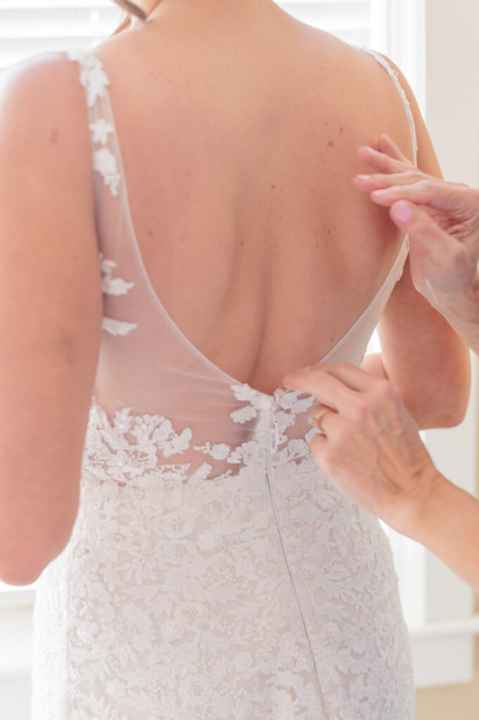 Bride adjusting delicate lace wedding gown straps, part of getting ready photos in Connecticut wedding photography timeline by Jennifer Nichole.