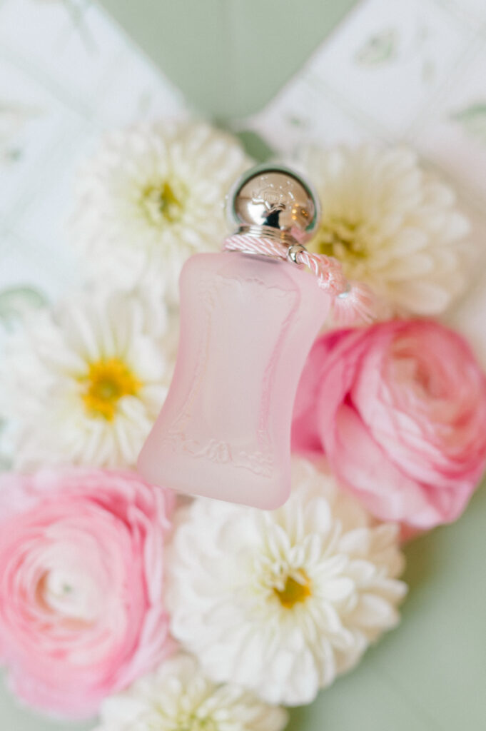 Soft pink bridal perfume bottle styled with ranunculus and white mums for romantic wedding detail photography at TPC River Highlands.