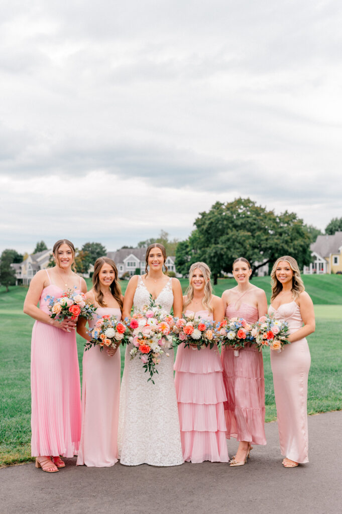 Bride with bridesmaids in pink dresses holding vibrant bouquets during romantic TPC Riverhighlands wedding.
