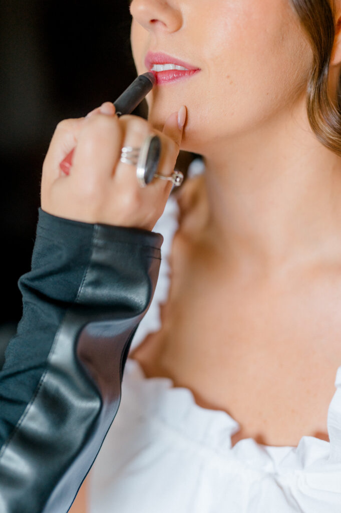 Bride applying pink lipstick during bridal prep, highlighting Connecticut wedding photography timeline detail shots by Jennifer Nichole.