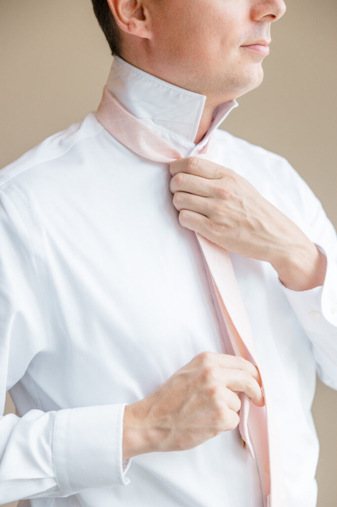 Groom tying blush pink necktie, captured during Connecticut wedding photography timeline getting ready moments by Jennifer Nichole.