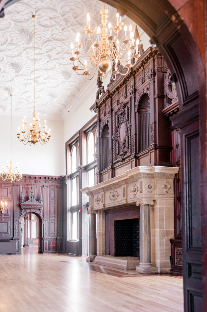 View through arched doorway to grand fireplace and chandeliers inside Branford House, ideal for elegant weddings
