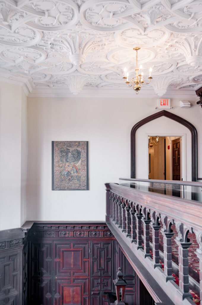 Historic upstairs landing with carved wood railing and antique tapestry at Branford House wedding venue