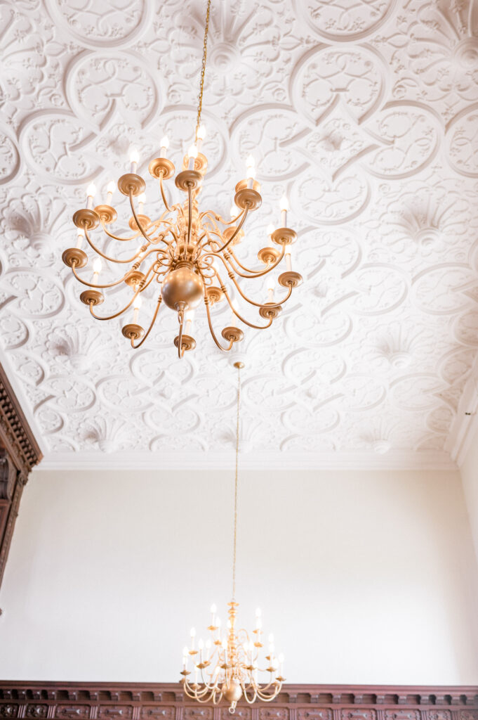 Ornate gold chandeliers hanging from the intricate white ceiling of Branford House wedding venue