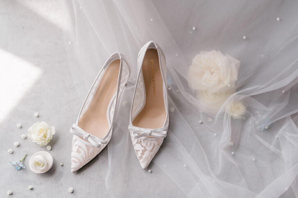 Blue and white coastal Newport wedding wedding featuring Stuart Weitzman lace heels surrounded by white florals. Details photographed flatlay-style by Newport wedding photographer Jennifer Nichole.