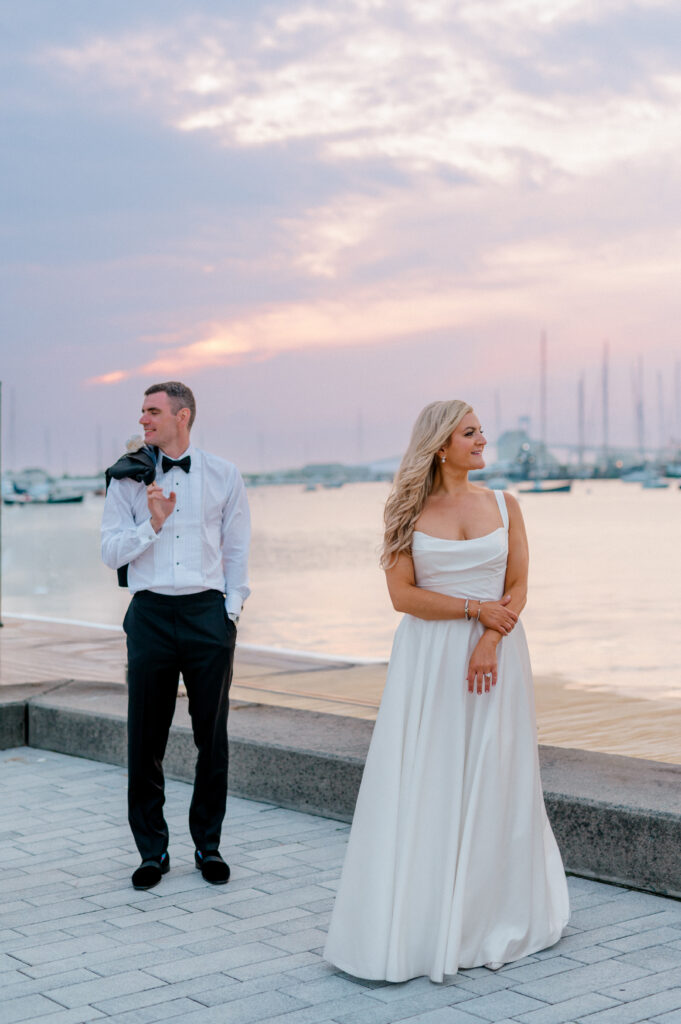 Bride and groom share romantic golden hour portraits by a marina, groom holding jacket over shoulder, bride in modern gown, captured at The Bohlin Newport by Jennifer Nichole.