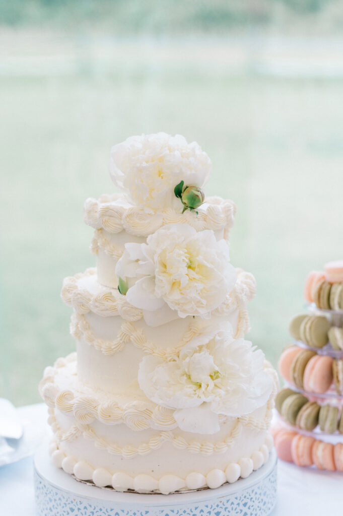 Close-up of elegant white tiered wedding cake with buttercream piping and fresh white peonies at a Smith Farm Gardens wedding.