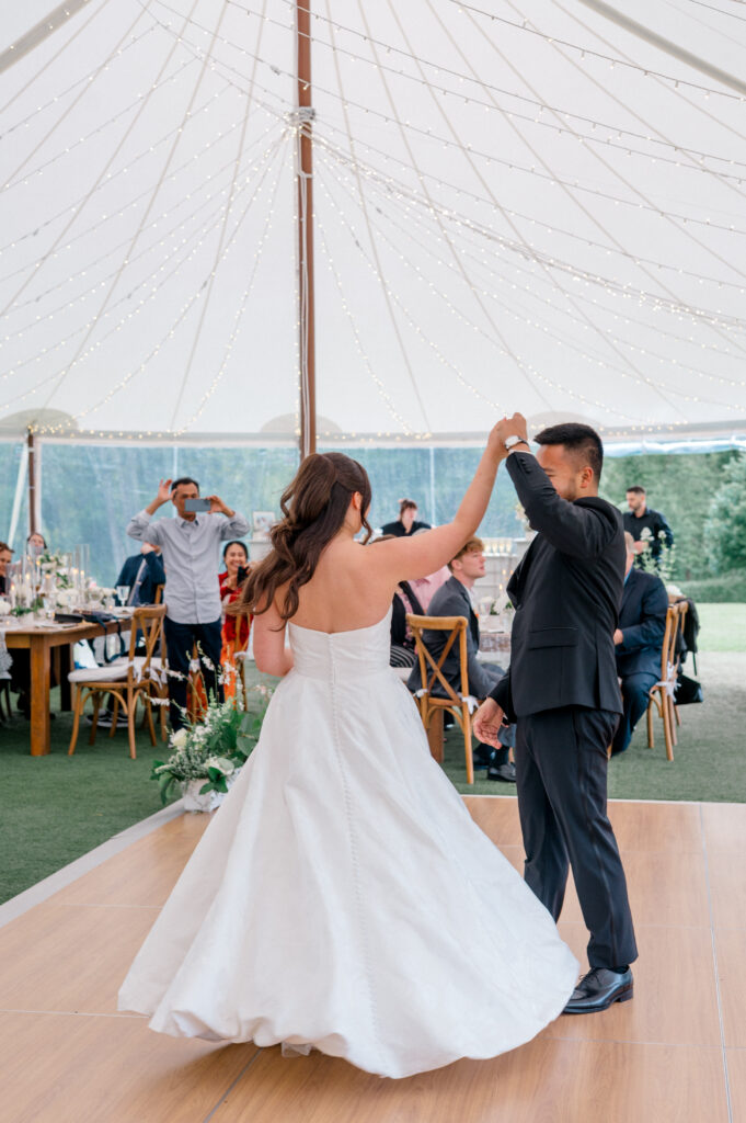 Groom twirls the bride during their first dance under fairy lights at Smith Farm Gardens wedding reception.