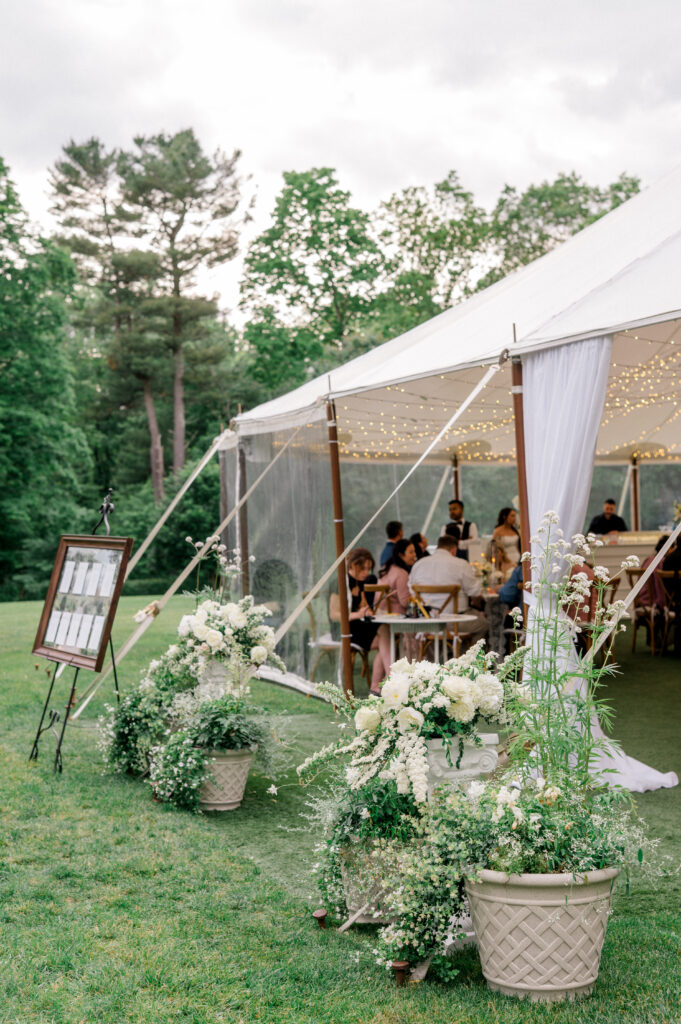 Romantic white floral arrangements and seating chart display welcome guests into the tented wedding reception at Smith Farm Gardens.