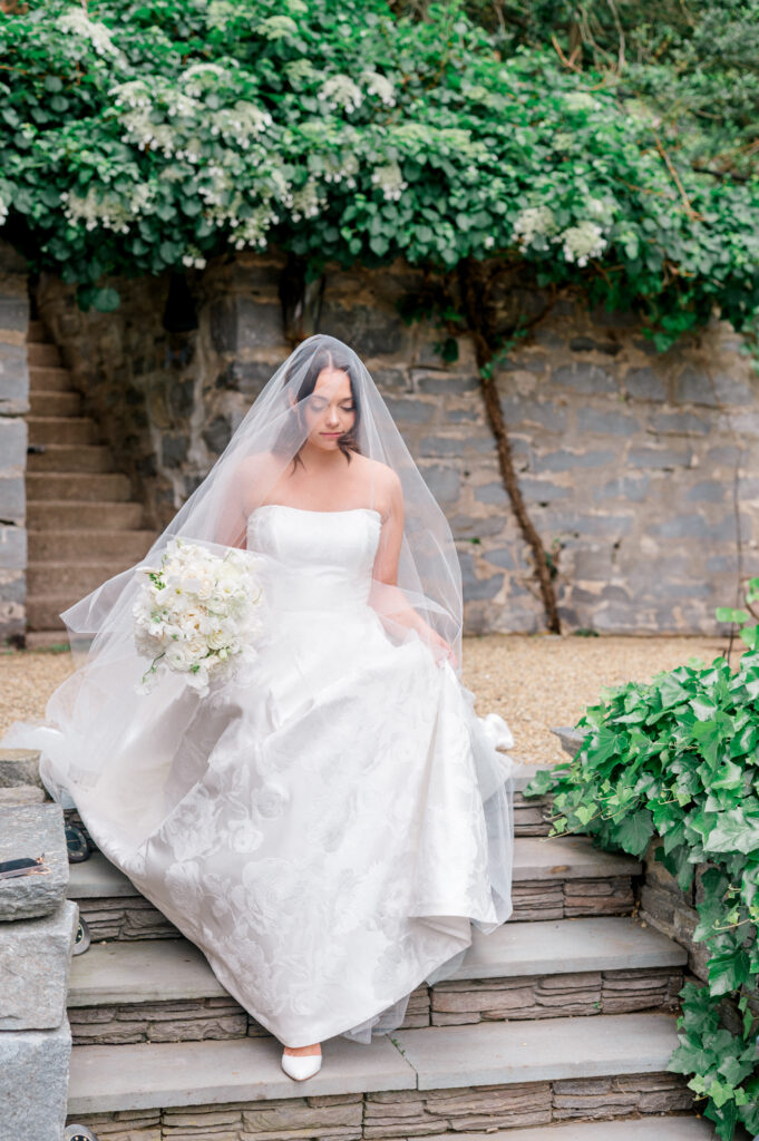 Bride walking down garden steps under a veil with a white bouquet at Smith Farm Gardens.