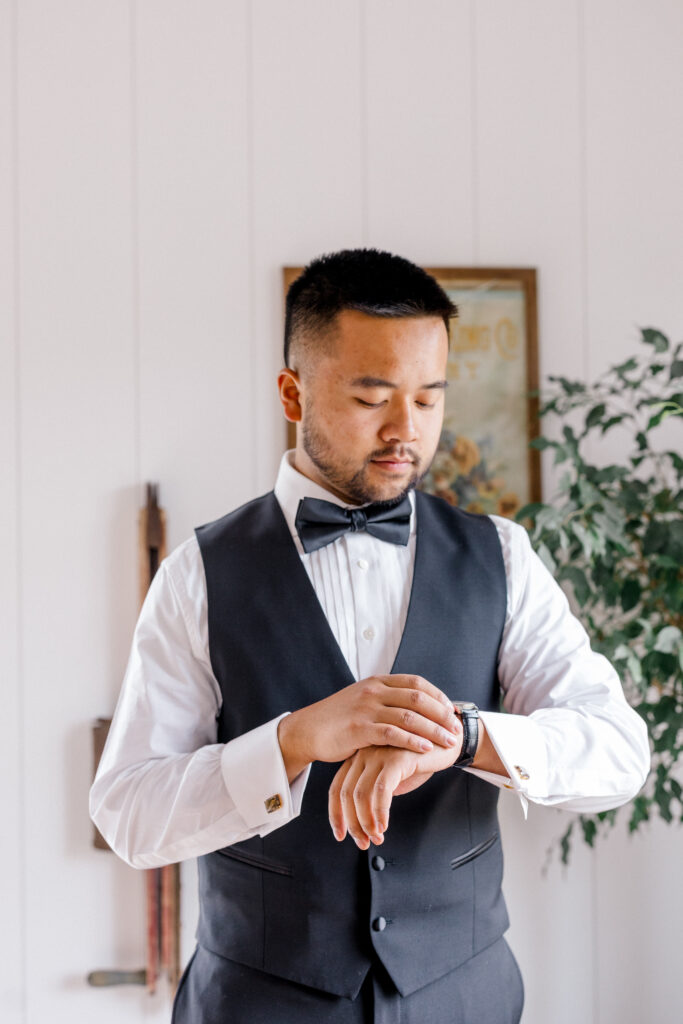 Groom standing by window in vest and bow tie preparing for his elegant Smith Farm Gardens wedding ceremony