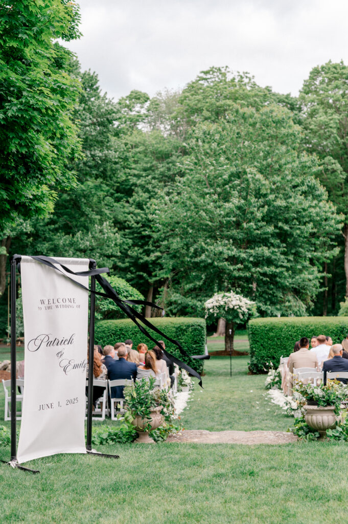 Elegant garden ceremony setup with welcome sign for Patrick and Emily’s June wedding, surrounded by lush greenery at Connecticut venue Smith Farm Gardens, photographed by Jennifer Nichole.