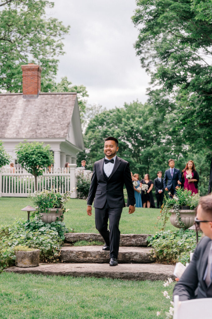 The groom walks down the garden steps toward the ceremony at Smith Farm Gardens, smiling at guests