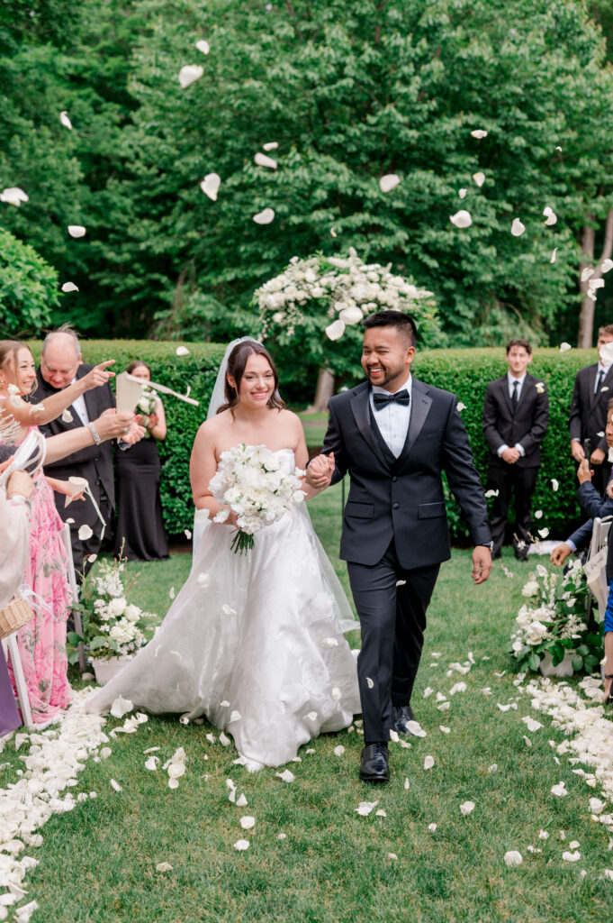 Emily and Patrick beam as they walk hand-in-hand through a shower of petals at their Smith Farm Gardens wedding