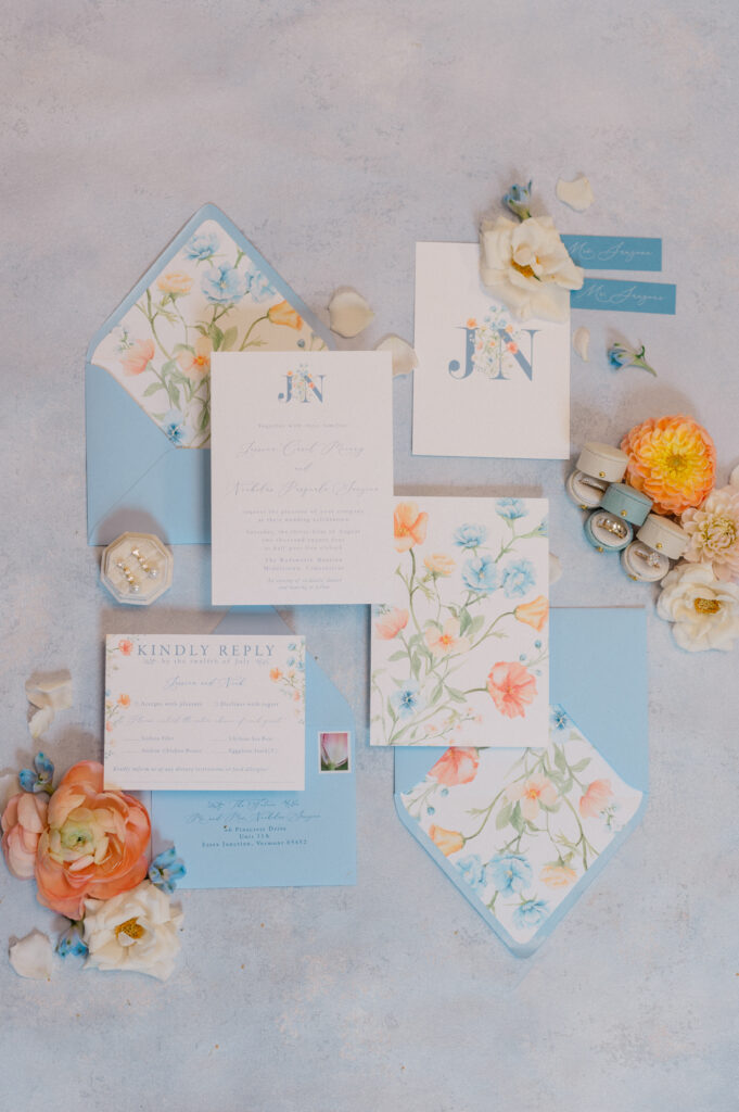 Floral watercolor invitation suite with blush and blue details, styled flatlay with ranunculus and ring boxes by Jennifer Nichole Photography.