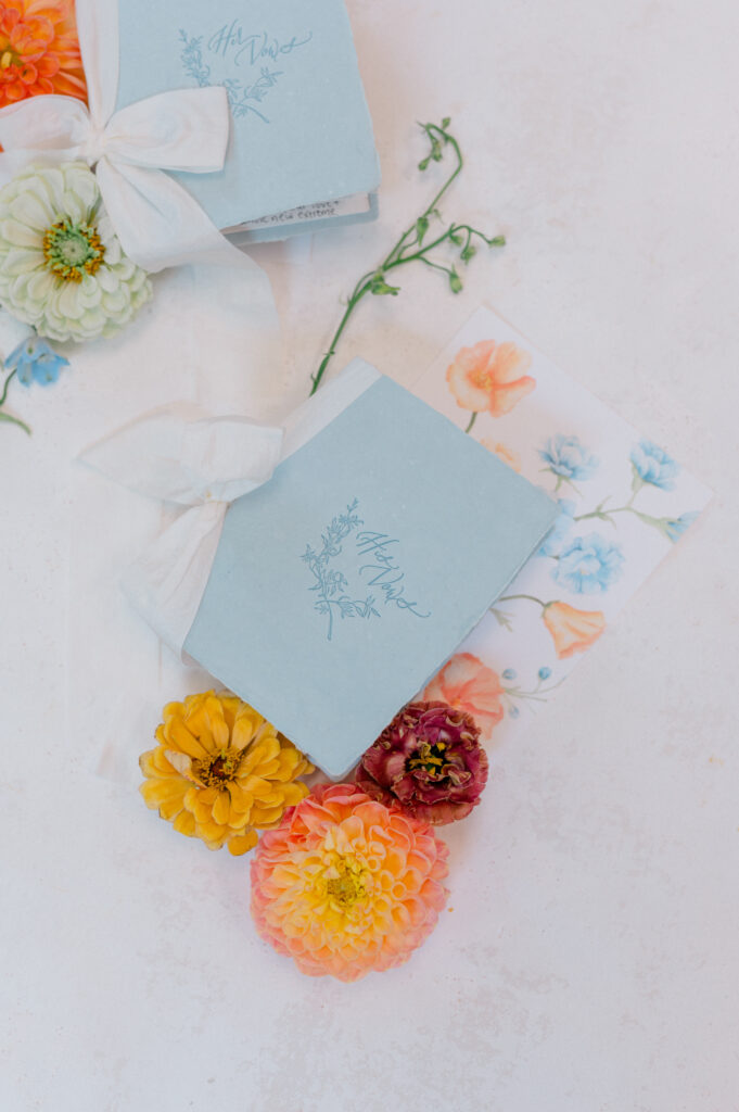 Powder blue vow books tied with silk ribbon and surrounded by bold summer blooms at Wadsworth Mansion wedding.