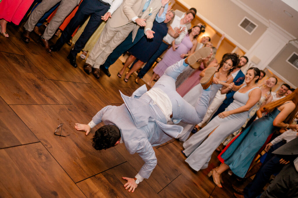 Groomsman breakdancing on the reception dance floor while guests cheer, a lively moment captured during the Connecticut wedding photography timeline by Jennifer Nichole.