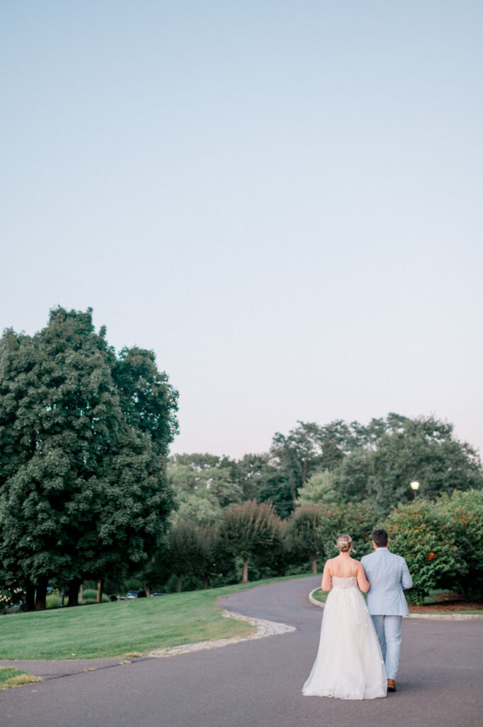 Bride and groom stroll down a winding path hand in hand at twilight, surrounded by trees and manicured gardens during their Connecticut wedding photographed by Jennifer Nichole.