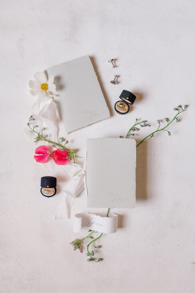 Flatlay of his and hers vow books with delicate florals and wedding rings, styled for a romantic wedding at Smith Farm Gardens.