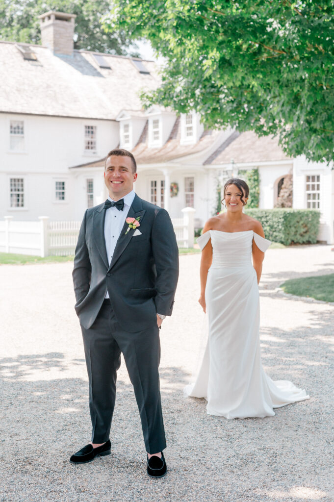 Smiling bride walks up behind groom for first look outside elegant Connecticut wedding venue
