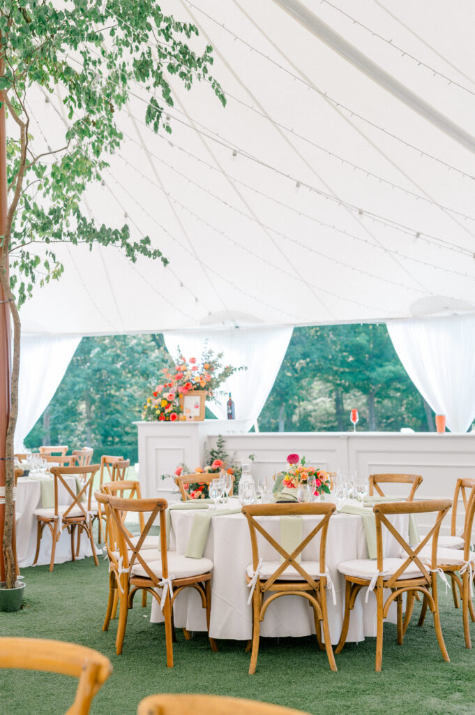 Bright tented Connecticut wedding reception featuring wooden cross-back chairs, vibrant floral centerpieces, and greenery accents, photographed for a wedding by Jennifer Nichole.